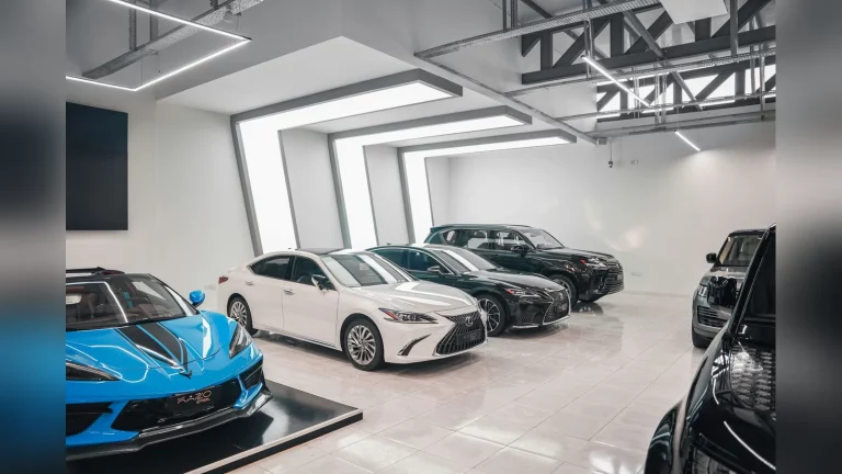 Қазақстандағы автосалондағы табиғи сәт: күнделікті киімдегі сатып алушы көлік жанында кеңесшімен құжаттарды талқылап тұр. Табиғи жарық, мәтін мен графикалық жазулар жоқ.