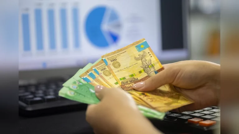 A Kazakhstan resident checks expenses on a smartphone at a kitchen table, with utility bills showing no legible details nearby. A candid everyday scene with no text or logos.