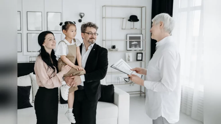 A family at a kitchen table in a city apartment in Kazakhstan, with adults reviewing household documents beside a laptop in natural daylight. An everyday scene with no text or readable personal data.