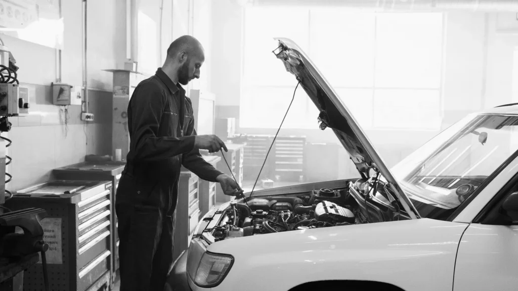 A driver beside their car at a vehicle inspection centre in Kazakhstan, with a diagnostic testing line and a staff member visible. Natural reportage photography, with no text.