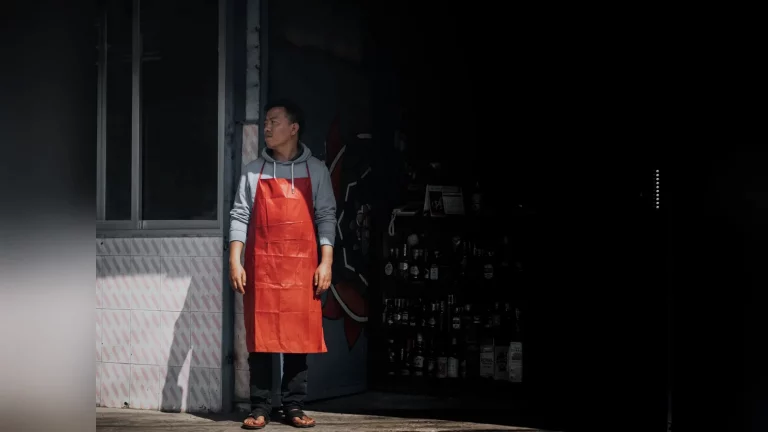 An entrepreneur behind the counter of a small shop in Kazakhstan on a typical working day, with goods on the shelves and natural light.